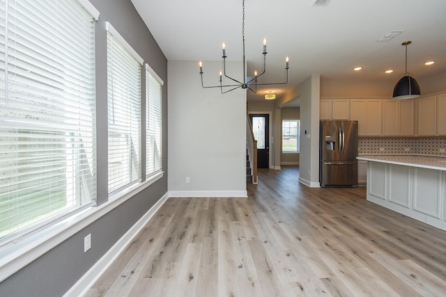 kitchen featuring decorative backsplash, stainless steel fridge, decorative light fixtures, a notable chandelier, and light hardwood / wood-style floors