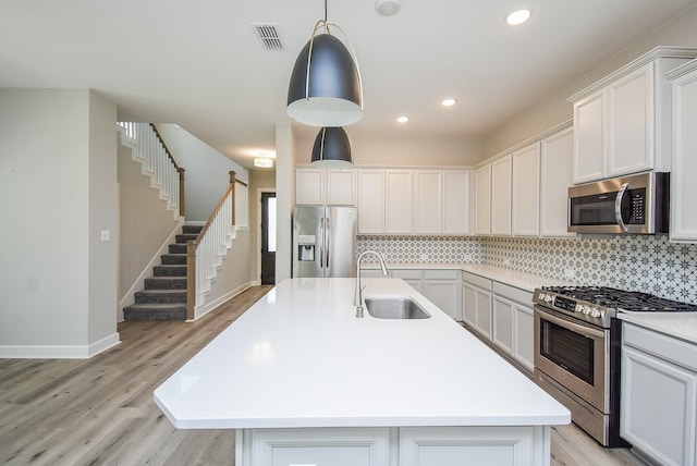 kitchen with sink, hanging light fixtures, an island with sink, white cabinets, and appliances with stainless steel finishes