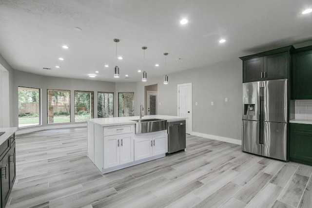 kitchen with a kitchen island with sink, sink, decorative light fixtures, light hardwood / wood-style floors, and stainless steel appliances