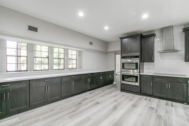 kitchen with tasteful backsplash, wall chimney exhaust hood, black electric cooktop, vaulted ceiling, and double oven