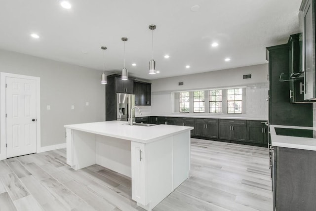 kitchen with sink, stainless steel fridge with ice dispenser, light hardwood / wood-style flooring, pendant lighting, and a center island with sink