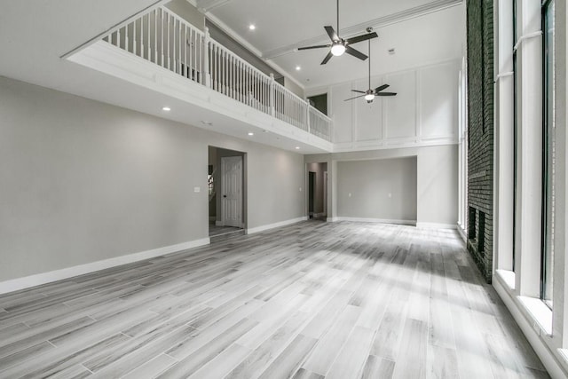 unfurnished living room with ceiling fan, a towering ceiling, light hardwood / wood-style floors, and a brick fireplace