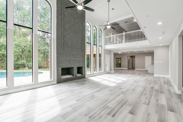 unfurnished living room featuring ceiling fan, a fireplace, a towering ceiling, and plenty of natural light