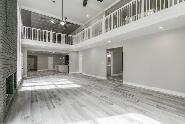 unfurnished living room featuring light wood-type flooring, a towering ceiling, a brick fireplace, and ceiling fan