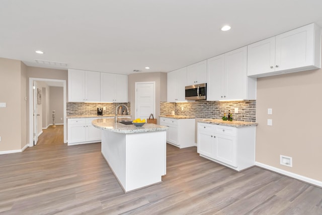 kitchen with white cabinetry, light stone countertops, an island with sink, and light hardwood / wood-style floors