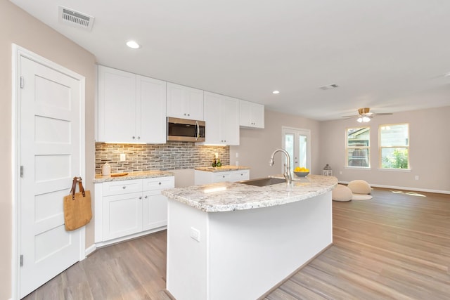 kitchen with a center island with sink, light wood-type flooring, sink, and white cabinets