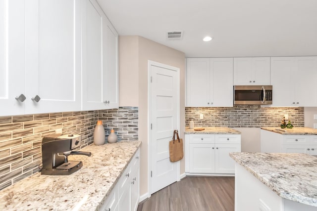 kitchen featuring light hardwood / wood-style flooring, white cabinetry, light stone counters, and decorative backsplash