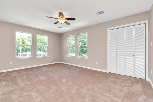 unfurnished bedroom featuring multiple windows, a closet, light colored carpet, and ceiling fan