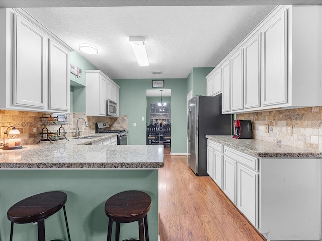 kitchen with white cabinetry, kitchen peninsula, stainless steel appliances, a kitchen breakfast bar, and sink