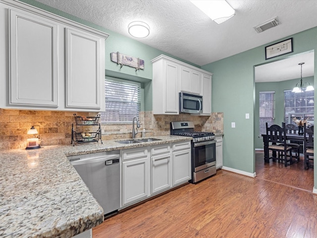 kitchen featuring stainless steel appliances, a notable chandelier, decorative light fixtures, white cabinets, and sink