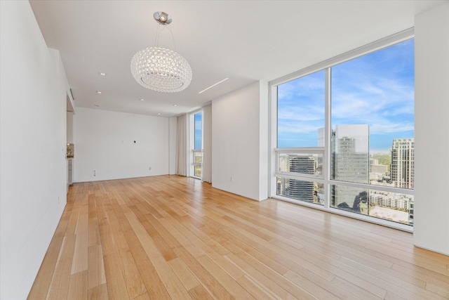 unfurnished room with expansive windows, a notable chandelier, and light hardwood / wood-style floors