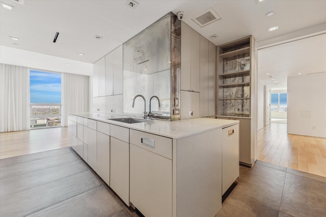 kitchen with light tile patterned floors, a kitchen island with sink, white cabinets, and sink