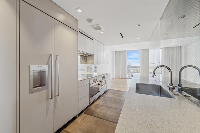 kitchen featuring black electric cooktop, built in fridge, white cabinets, light stone counters, and sink