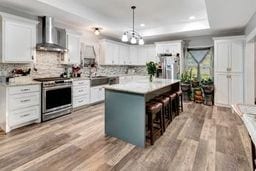 kitchen with white cabinets, a center island, stainless steel stove, and wall chimney range hood