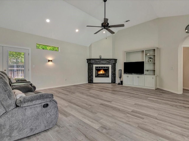 living room with light hardwood / wood-style floors, vaulted ceiling, ceiling fan, and a stone fireplace