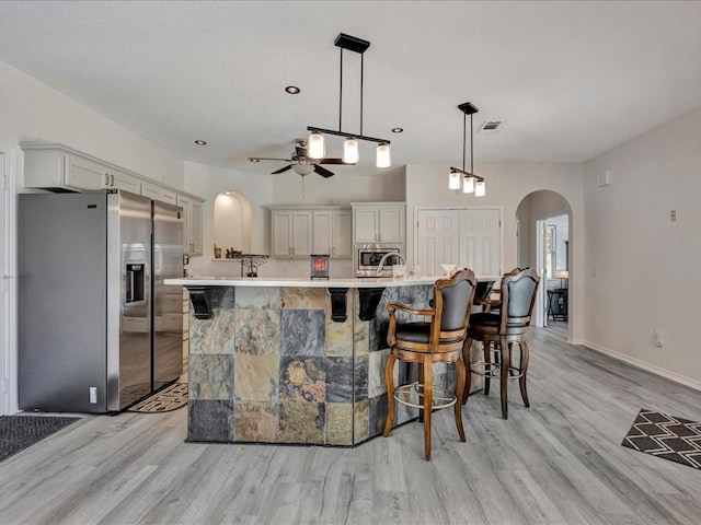 kitchen with stainless steel appliances, ceiling fan, hanging light fixtures, a breakfast bar area, and an island with sink