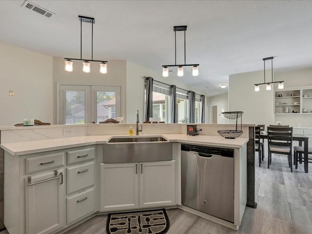 kitchen featuring stainless steel dishwasher, sink, hanging light fixtures, and light hardwood / wood-style flooring