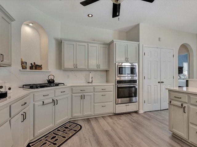 kitchen featuring light wood-type flooring, tasteful backsplash, stainless steel appliances, ceiling fan, and white cabinetry