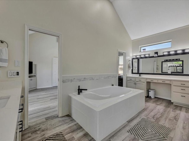 bathroom featuring vanity, a relaxing tiled tub, wood-type flooring, and high vaulted ceiling