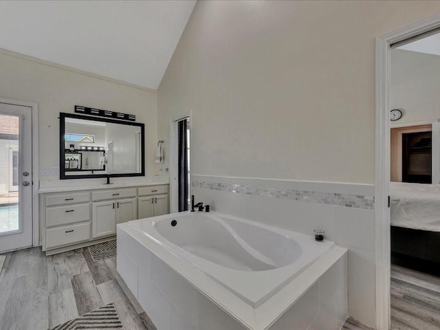 bathroom featuring hardwood / wood-style floors, vanity, a relaxing tiled tub, and lofted ceiling