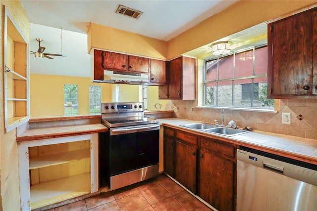 kitchen with tile countertops, backsplash, sink, ceiling fan, and stainless steel appliances