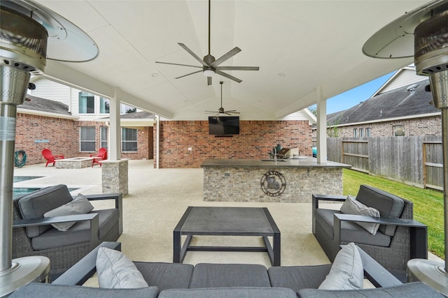 view of patio with ceiling fan, exterior bar, and an outdoor living space with a fire pit