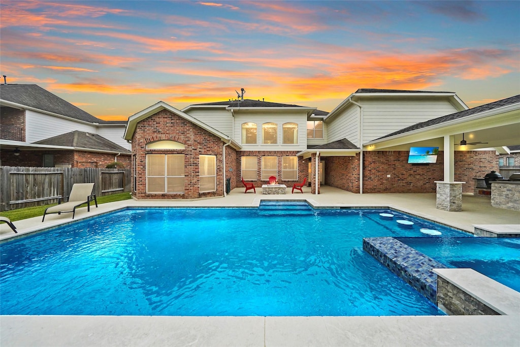 pool at dusk with pool water feature, an outdoor fire pit, and a patio area