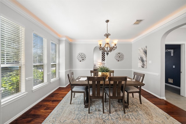 dining space with dark wood-type flooring, ornamental molding, and an inviting chandelier