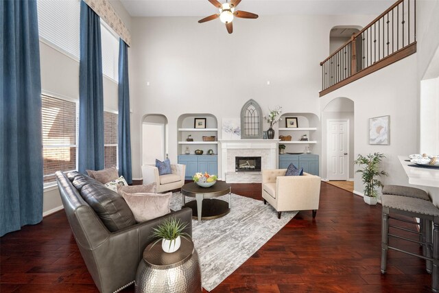 living room with dark wood-type flooring, built in features, ceiling fan, and a towering ceiling