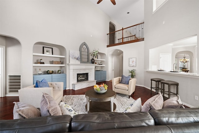 living room featuring wood-type flooring, ceiling fan with notable chandelier, built in features, and a fireplace