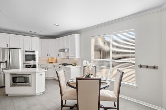 kitchen with a breakfast bar, white cabinetry, stainless steel appliances, ornamental molding, and a kitchen island