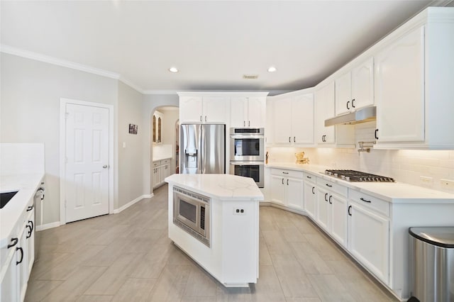 kitchen featuring appliances with stainless steel finishes, a center island, ornamental molding, white cabinets, and decorative backsplash