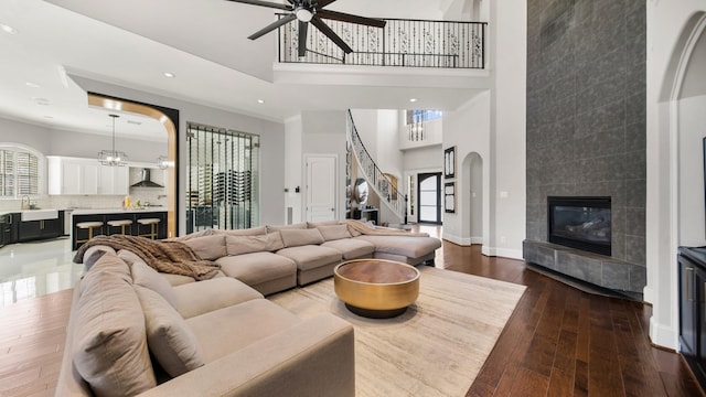 living room with hardwood / wood-style floors, a high ceiling, a tiled fireplace, ceiling fan, and sink