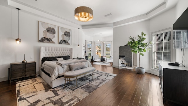 bedroom featuring crown molding, an inviting chandelier, dark hardwood / wood-style floors, and a stone fireplace