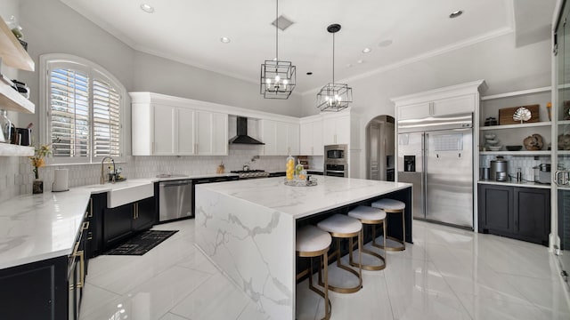 kitchen with white cabinets, a center island, wall chimney range hood, and built in appliances