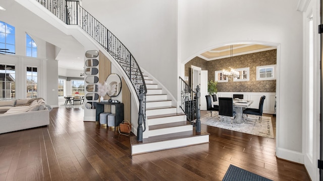 foyer with a high ceiling, dark wood-type flooring, an inviting chandelier, and crown molding