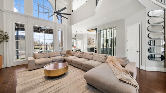 living room featuring a towering ceiling, ceiling fan with notable chandelier, and wood-type flooring