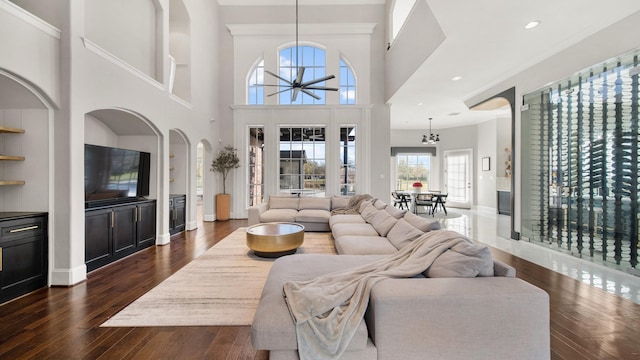 living room with a towering ceiling, dark hardwood / wood-style flooring, an inviting chandelier, and built in shelves