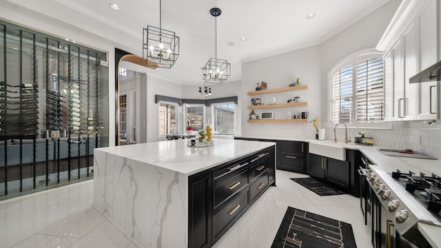 kitchen featuring light stone counters, decorative light fixtures, a kitchen island, white cabinets, and sink