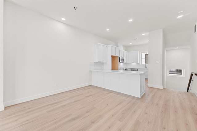 kitchen featuring kitchen peninsula, decorative backsplash, light hardwood / wood-style flooring, range, and white cabinetry