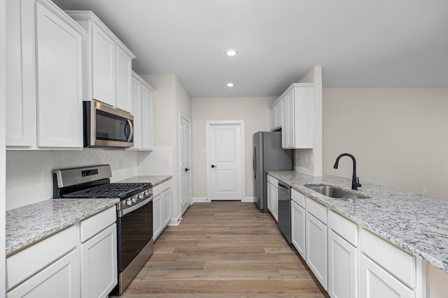 kitchen with sink, stainless steel appliances, light stone counters, light hardwood / wood-style flooring, and white cabinets