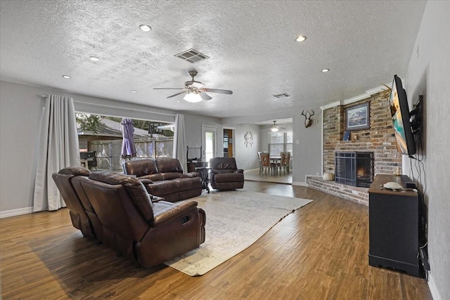 living room with a textured ceiling, ceiling fan, dark wood-type flooring, and a brick fireplace