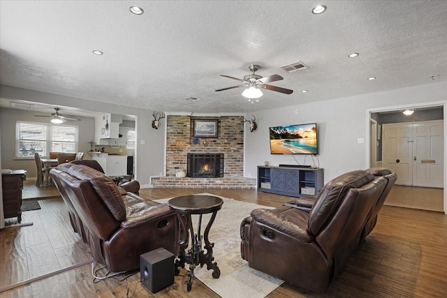 living room with a fireplace, a textured ceiling, hardwood / wood-style flooring, and ceiling fan