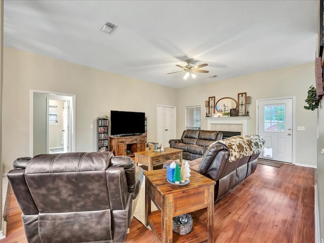 living room with ceiling fan, wood-type flooring, and a tile fireplace