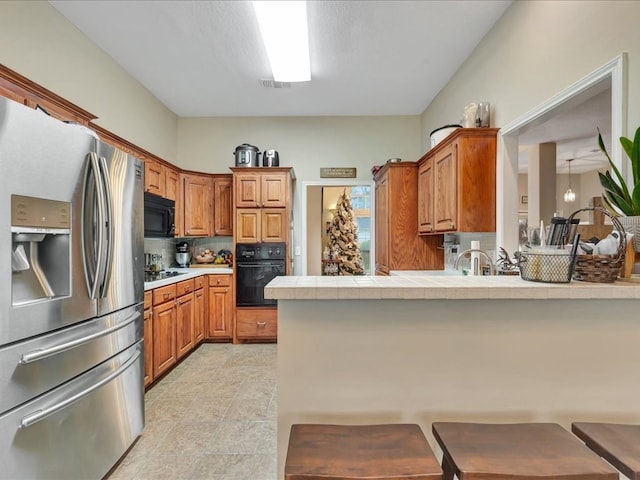 kitchen featuring backsplash, black appliances, a textured ceiling, tile counters, and kitchen peninsula