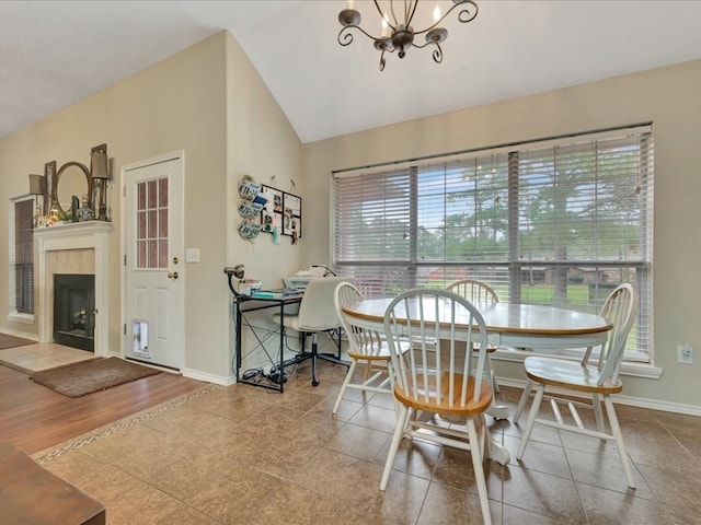 tiled dining space featuring a tiled fireplace, a chandelier, and vaulted ceiling