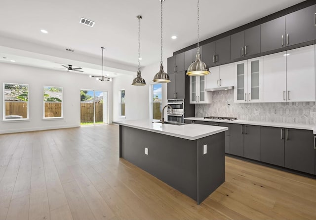 kitchen featuring backsplash, white cabinets, ceiling fan, an island with sink, and decorative light fixtures