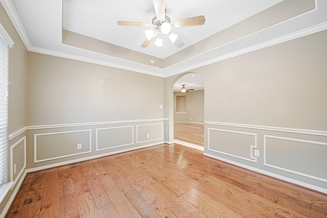 empty room featuring a raised ceiling, light hardwood / wood-style flooring, ceiling fan, and crown molding