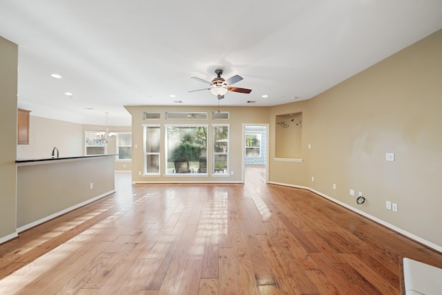 unfurnished living room with ceiling fan with notable chandelier, sink, and light hardwood / wood-style flooring