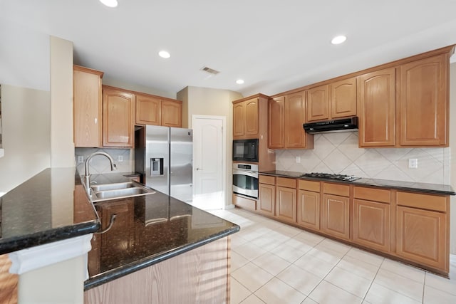 kitchen featuring sink, backsplash, dark stone countertops, light tile patterned flooring, and appliances with stainless steel finishes